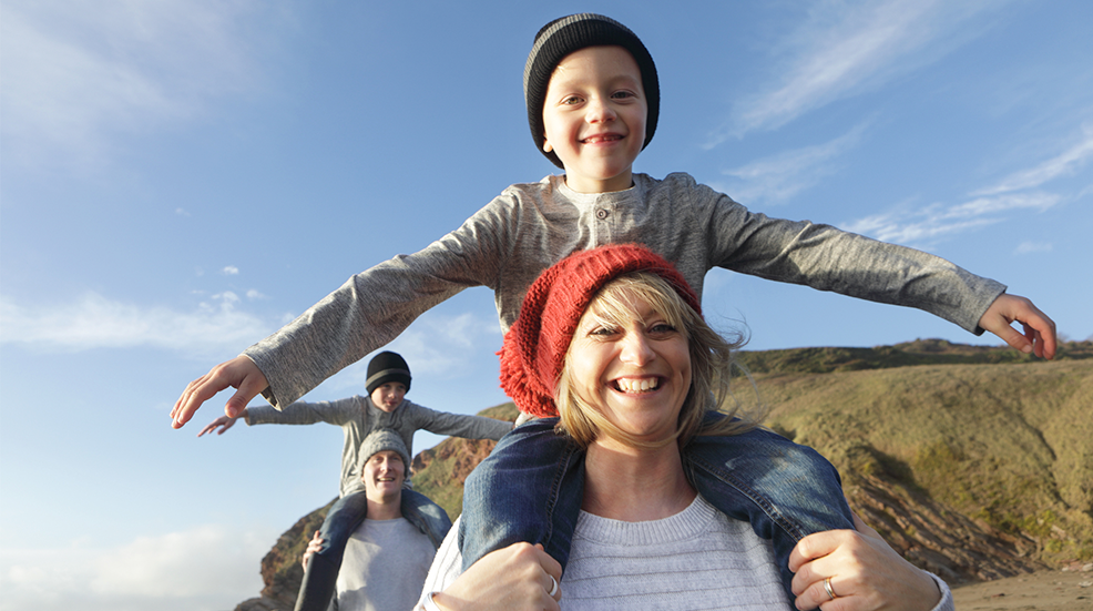Family on beach in winter, mother giving son piggyback